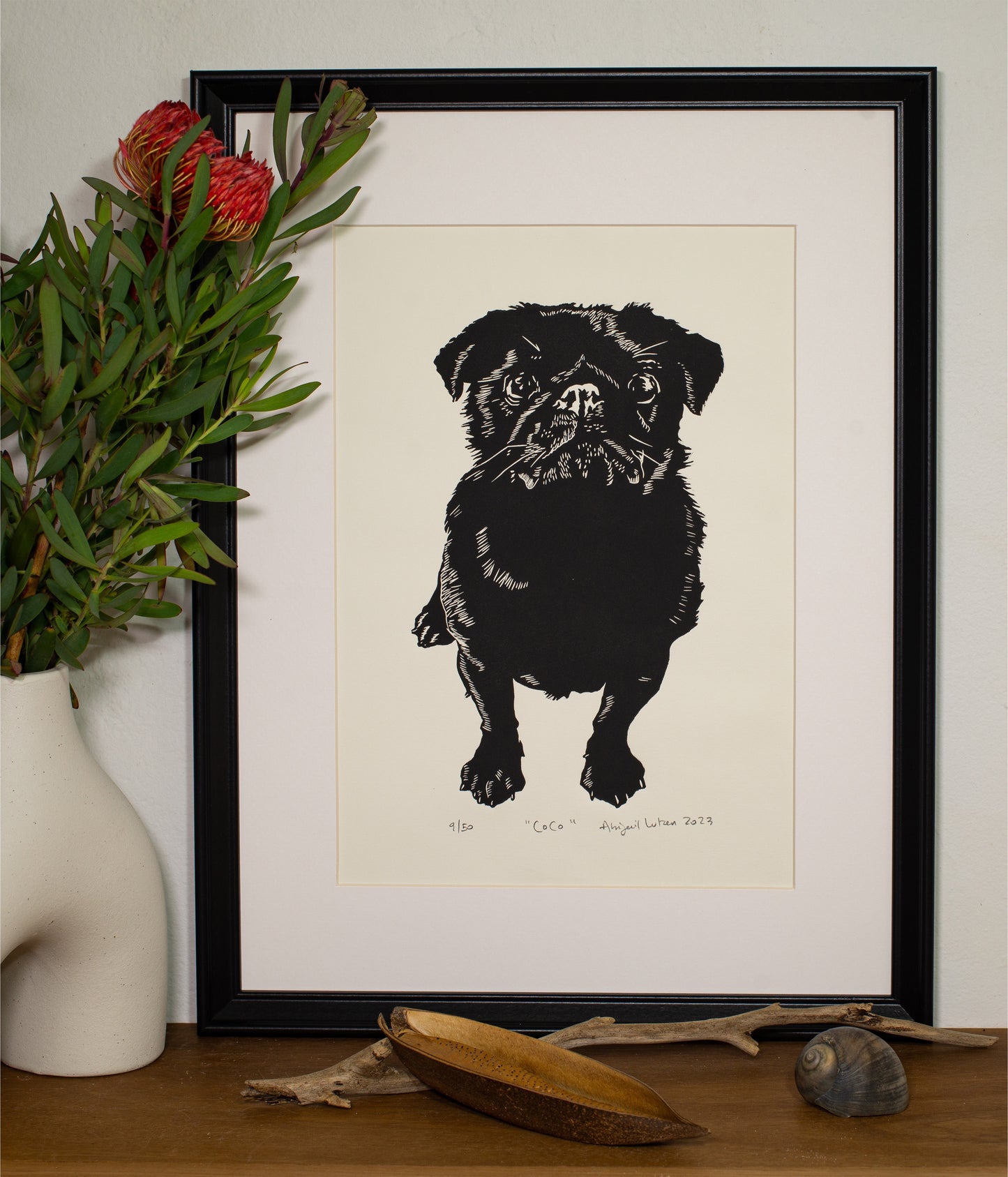 The Coco linocut in a black frame, beside a vase of native flowers