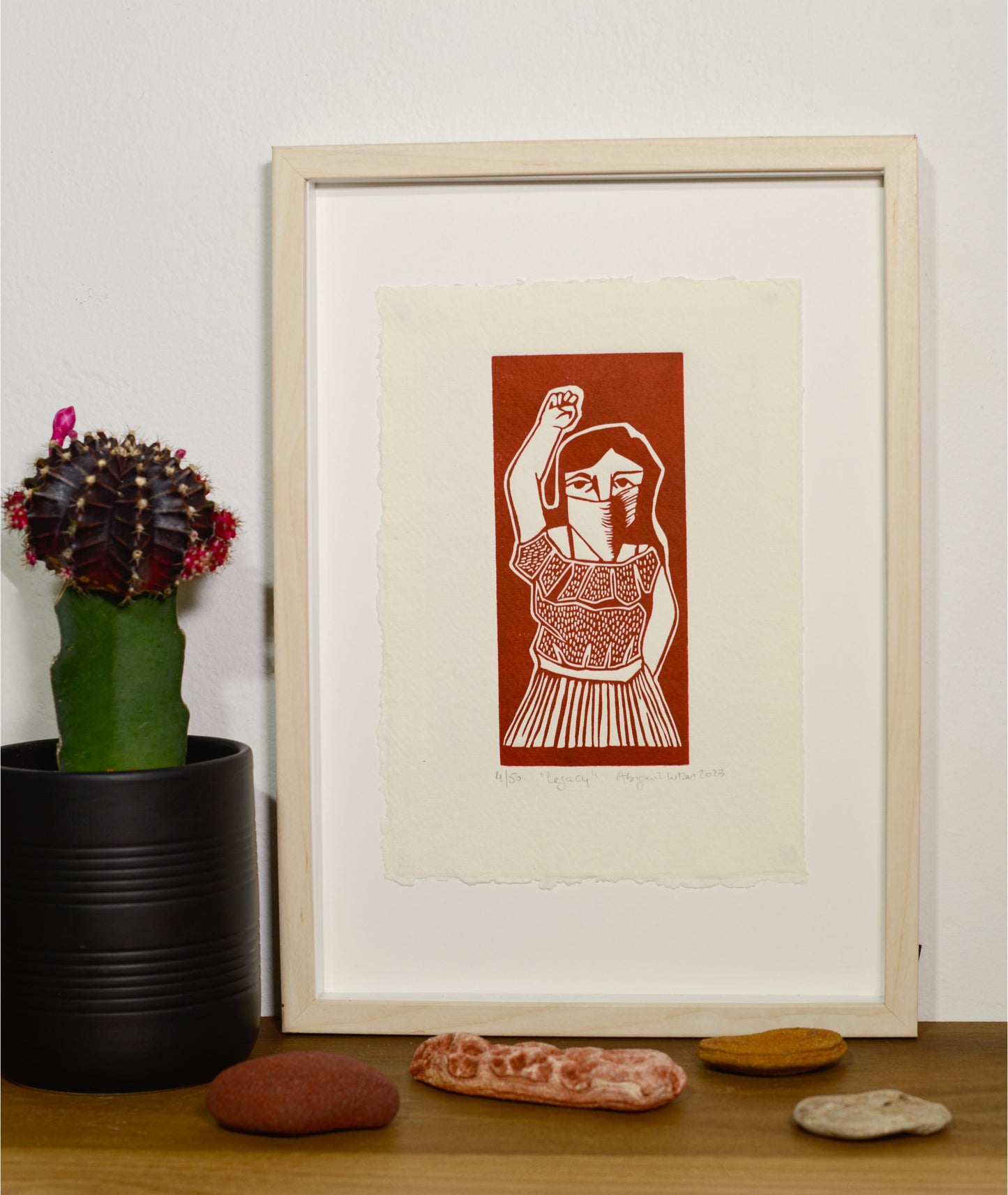 The Legacy linocut in a white frame, beside a potted plant