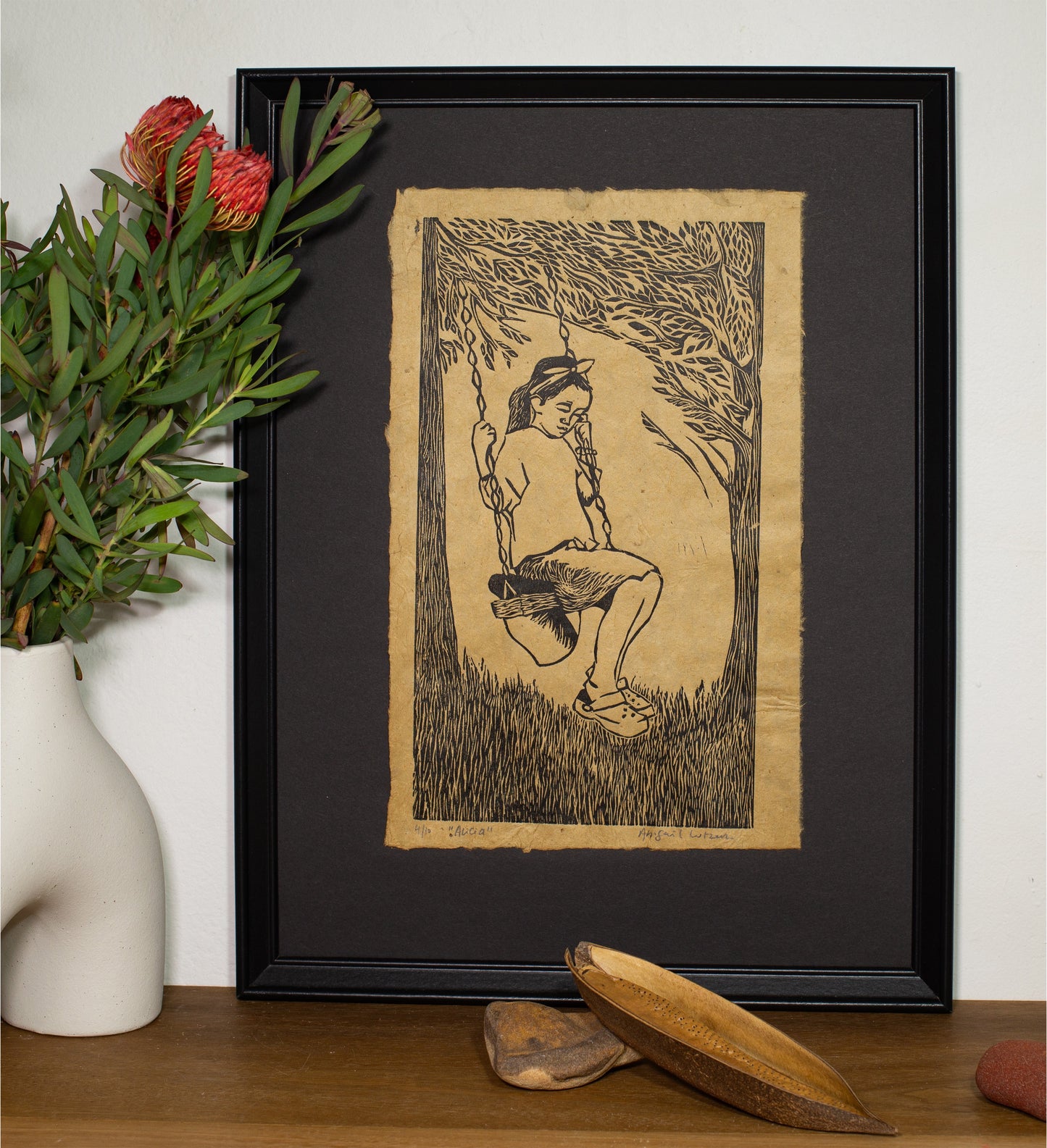 The Alicia linocut in a black frame, beside a vase of native foliage