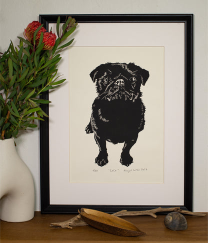 The Coco linocut in a black frame, beside a vase of native flowers