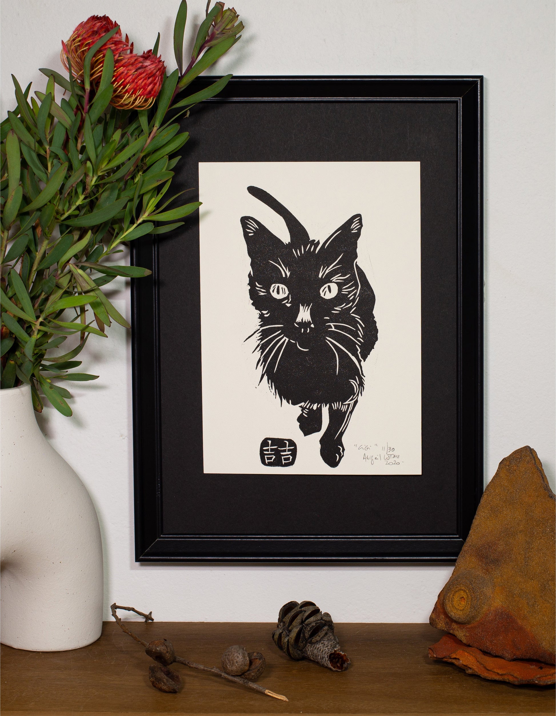 The Gigi linocut in a black frame, beside a vase of native flowers