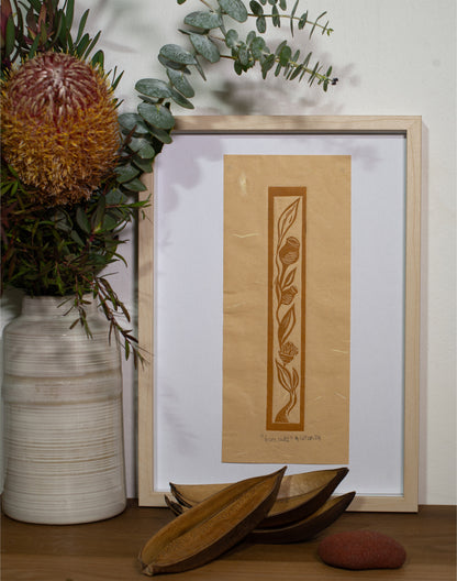 The Gumnuts linocut in a pale frame, beside a vase of native flowers