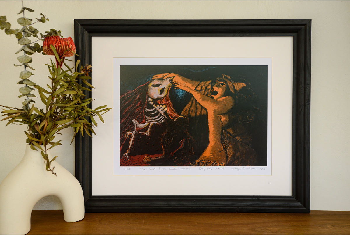 The La Loba linocut in a black frame with a wide mount, beside a vase of native flowers