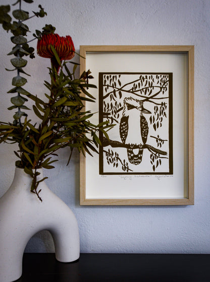 Laughing Kookaburra linocut print, framed on a wall beside a banksia