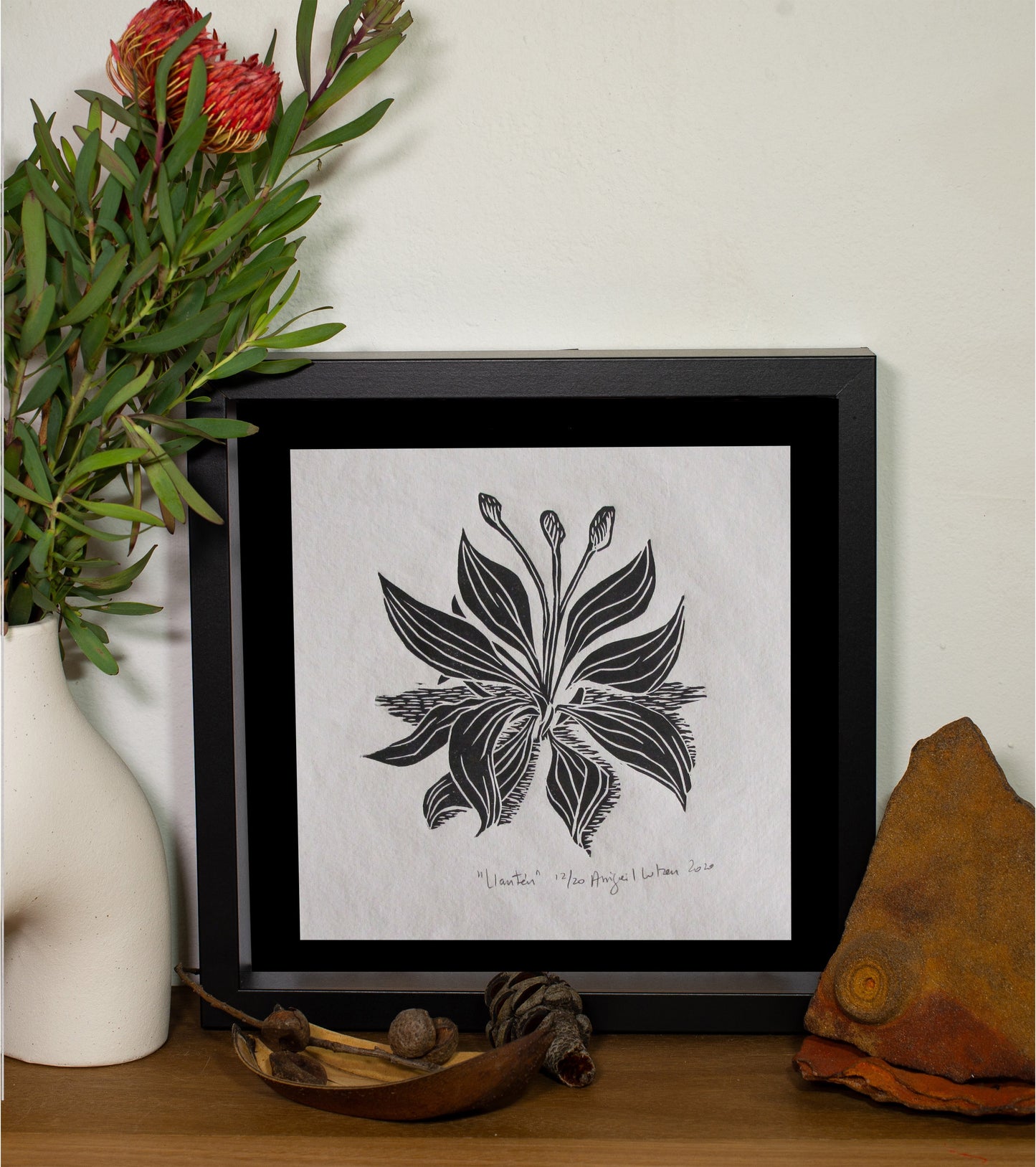 The Llanten linocut in a black frame, beside a vase of native flowers