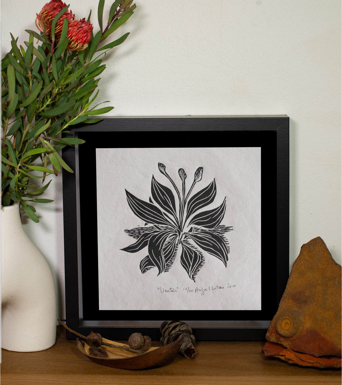 The Llanten linocut in a black frame, beside a vase of native flowers