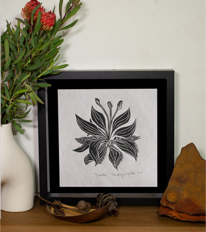 The Llanten linocut in a black frame, beside a vase of native flowers