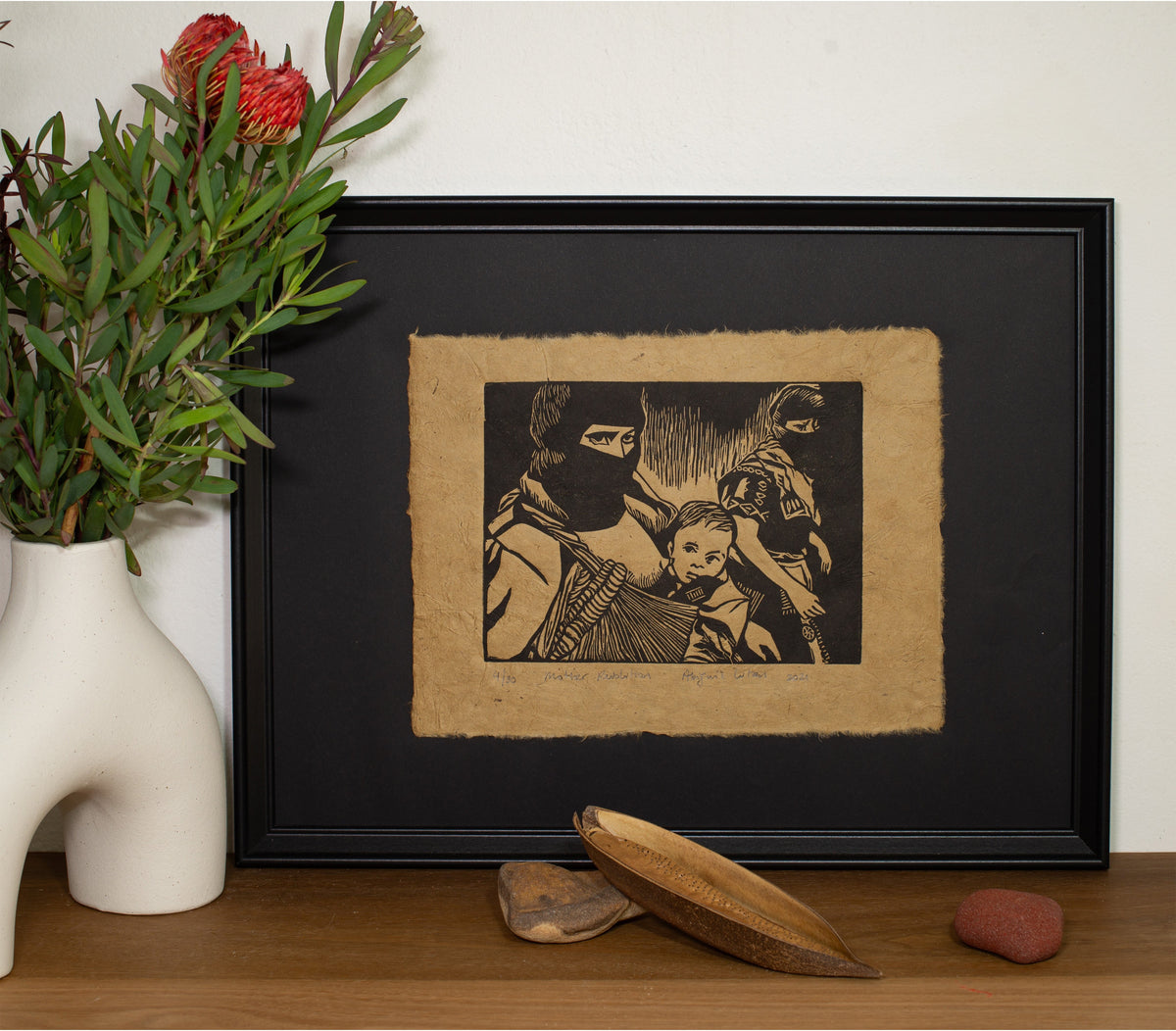 The Mother Revolution linocut in a black frame, beside a vase of native flowers