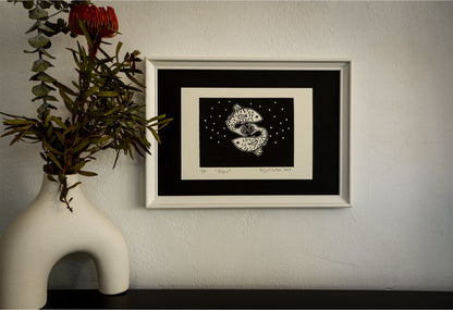 The Piscis linocut in a pale frame, beside a vase of native flowers