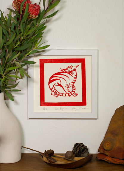 The Red Tiger linocut framed on a wall beside a vase of native flowers
