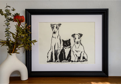 The Rocky, Sootie and Bluebelle linocut in a black frame, beside a vase of native flowers