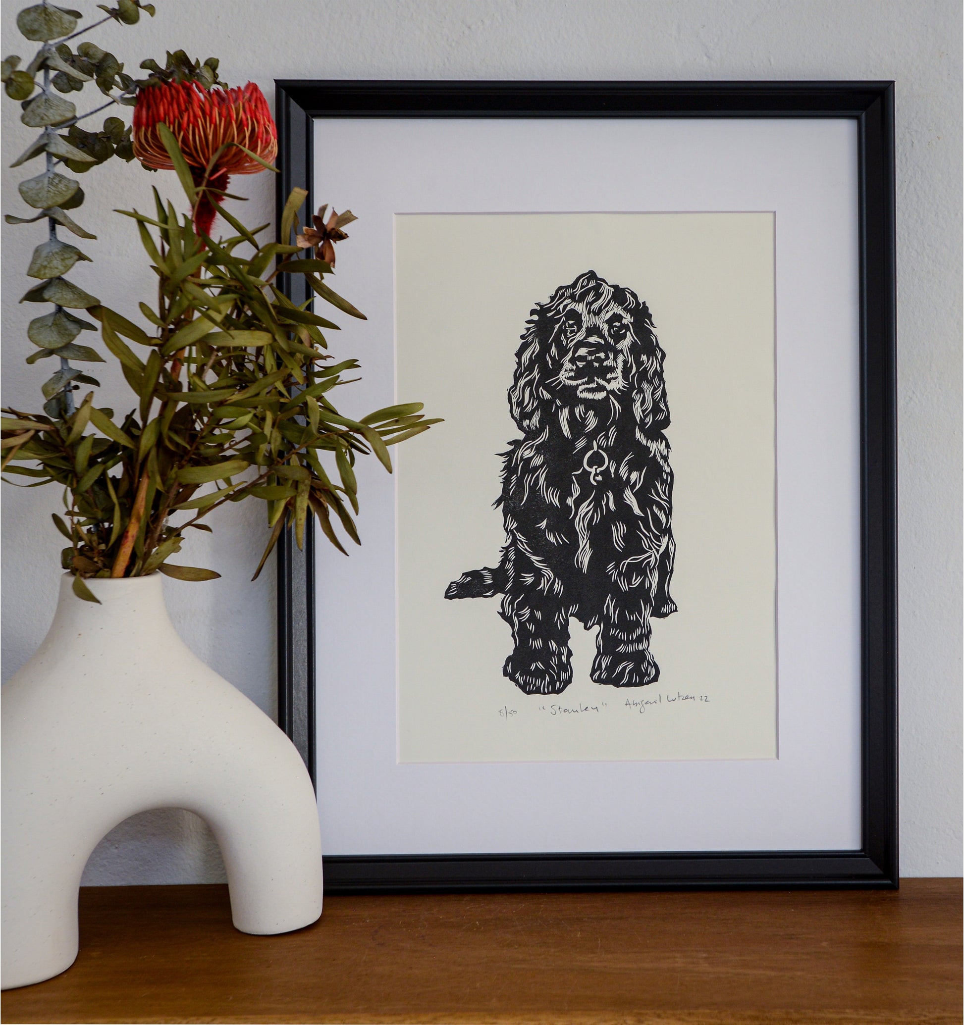 The Stanley linocut in a black frame, beside a vase of native flowers