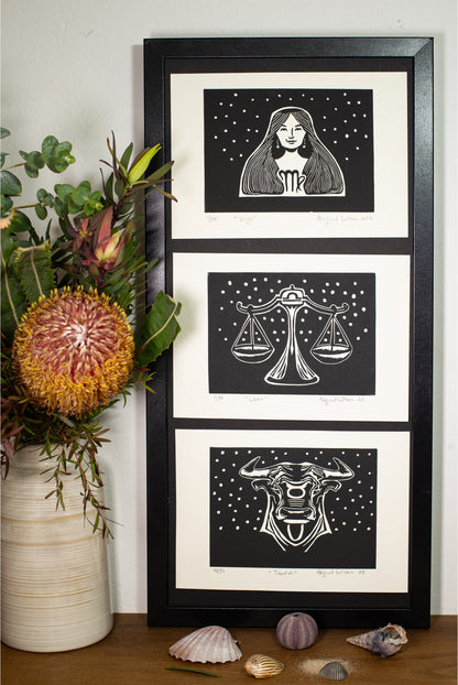The Taurus linocut in a black frame, beside a vase of native flowers