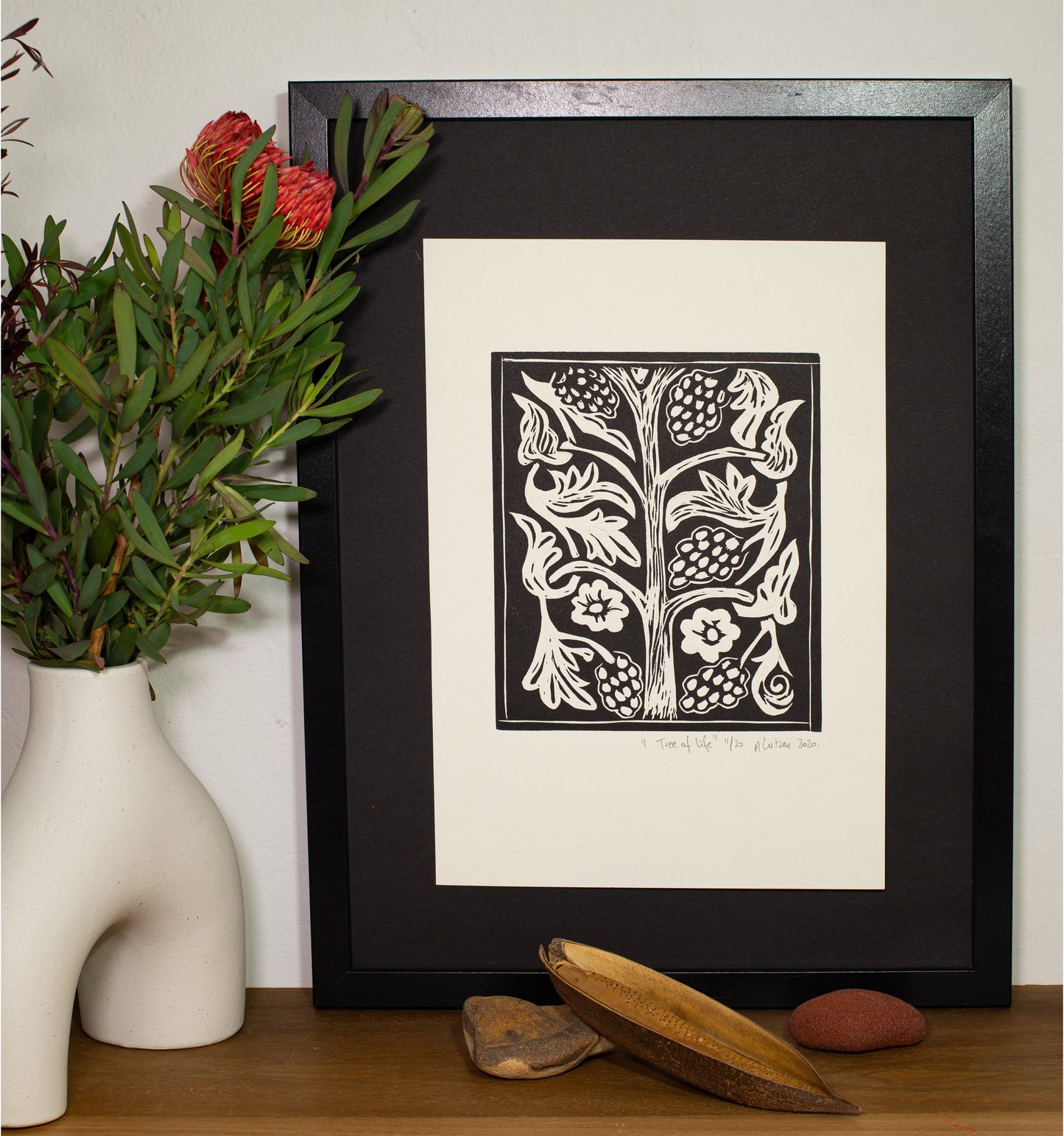 The Tree of Life linocut in a dark frame, beside a vase of native foliage