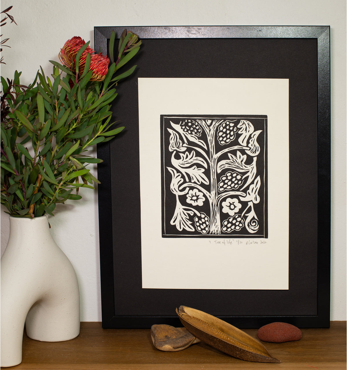 The Tree of Life linocut in a dark frame, beside a vase of native foliage